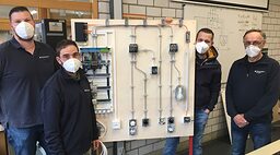 Florian Kuolt mit 3 Ausbildern der Elektro-Abteilung in einer Elektro-Werkstatt vor einer mobilen Schalttafel
